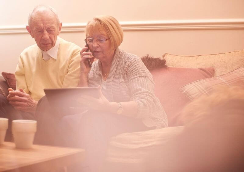 Woman helping man on a tablet and phone to insurer